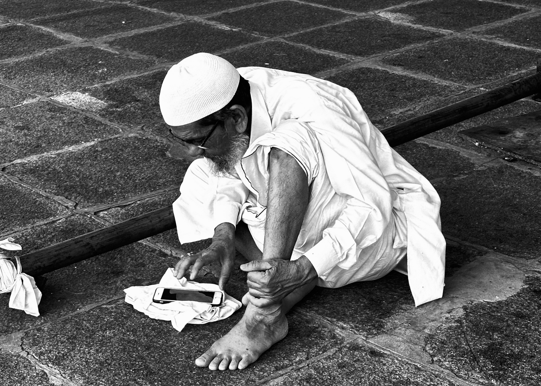 Elderly man in white clothing and cap sitting on stone steps using mobile phone - contemporary street portrait photography