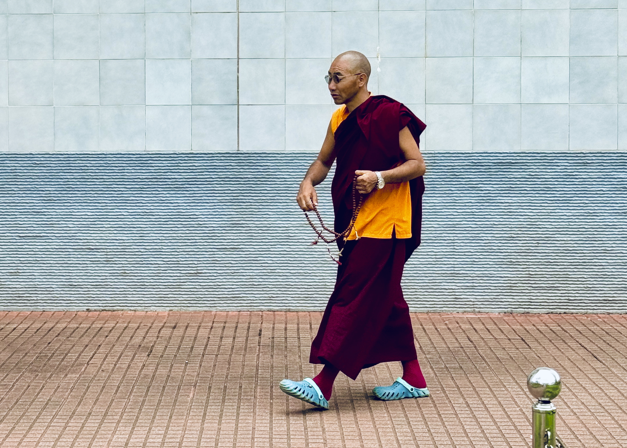 Buddhist monk in maroon and yellow robes walking on brick pathway - spiritual street photography