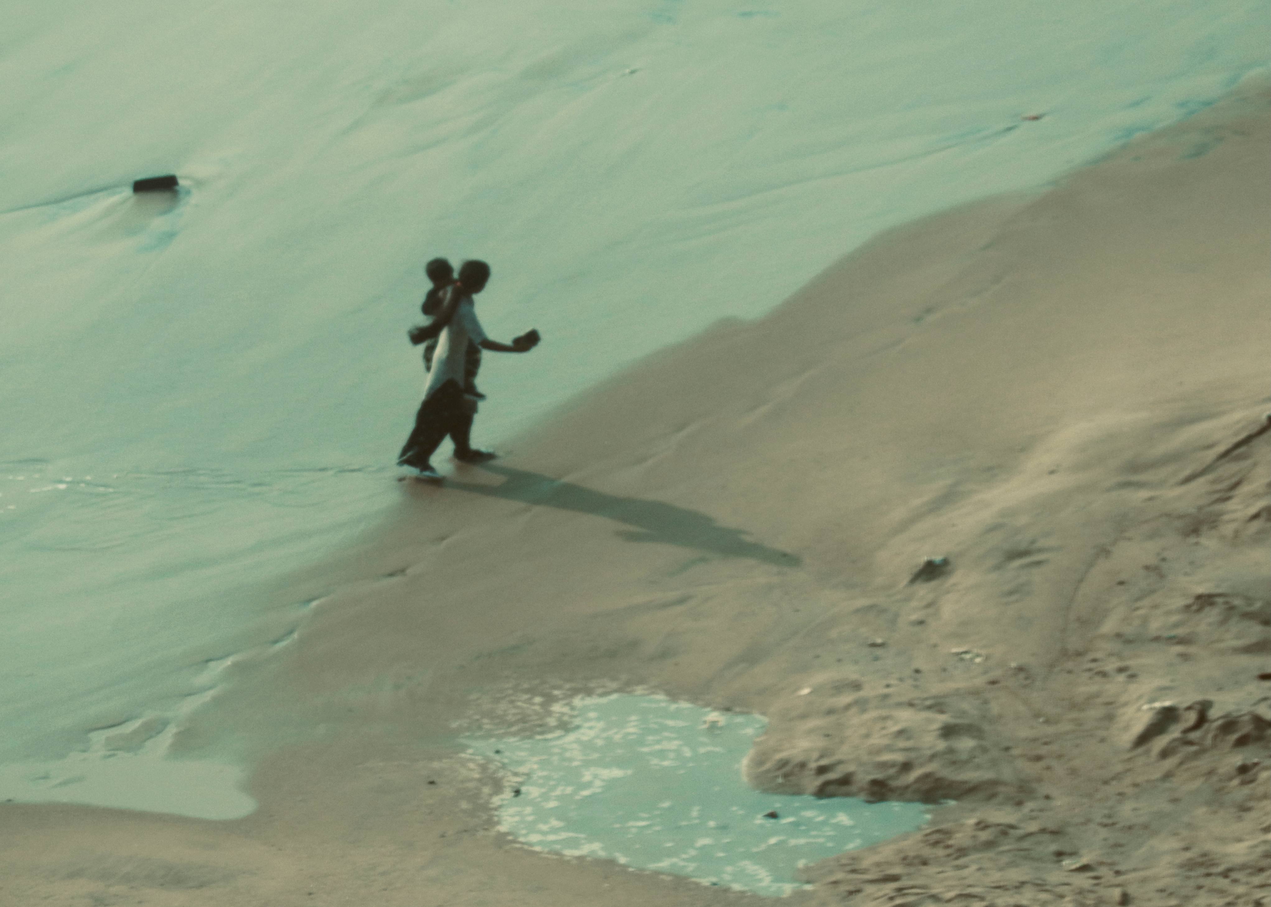 Parent carrying child in turquoise shallow water - intimate family beach moment photography