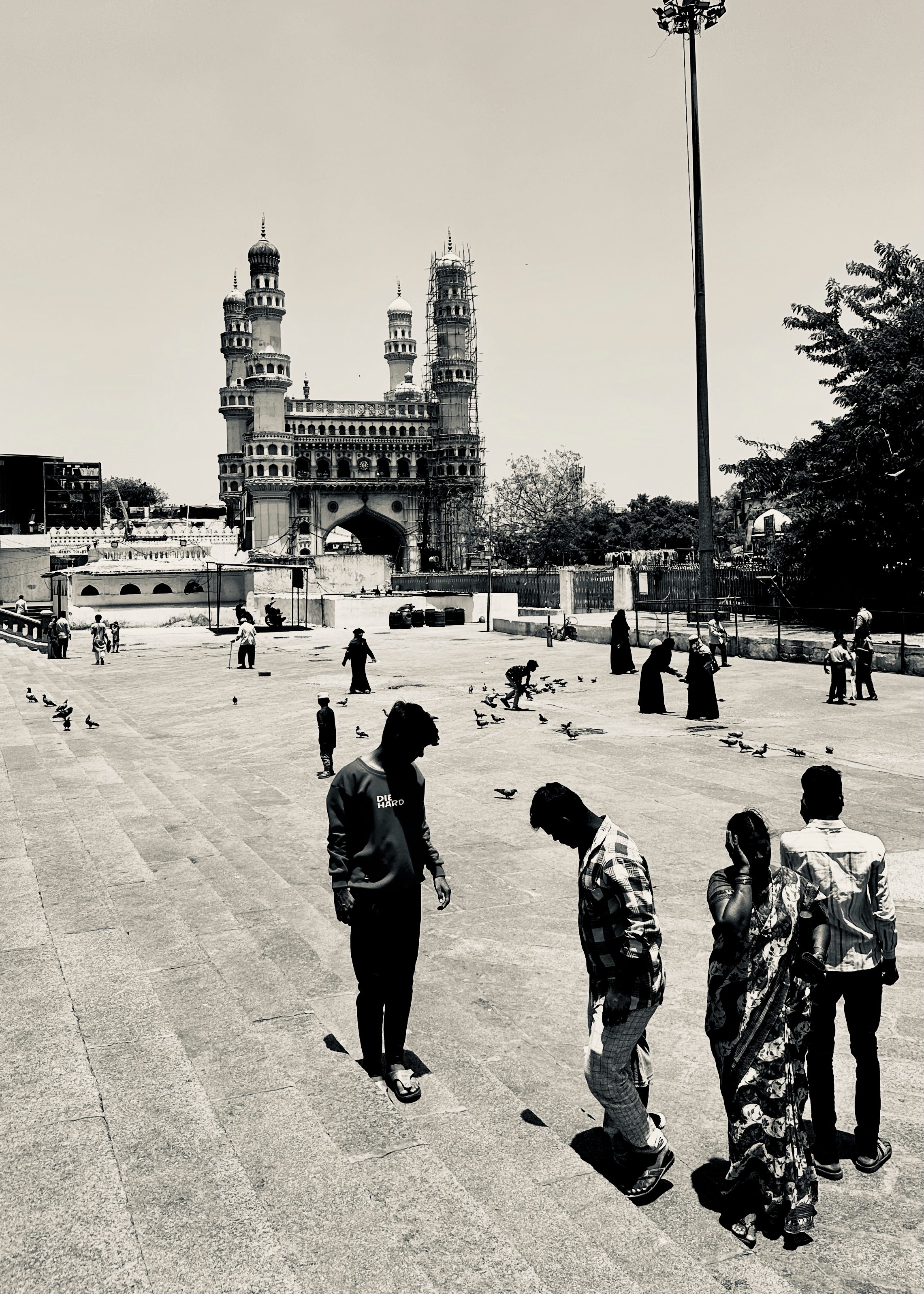 Black and white street scene with people gathered in courtyard before historic mosque with minarets - Hyderabad architecture photography
