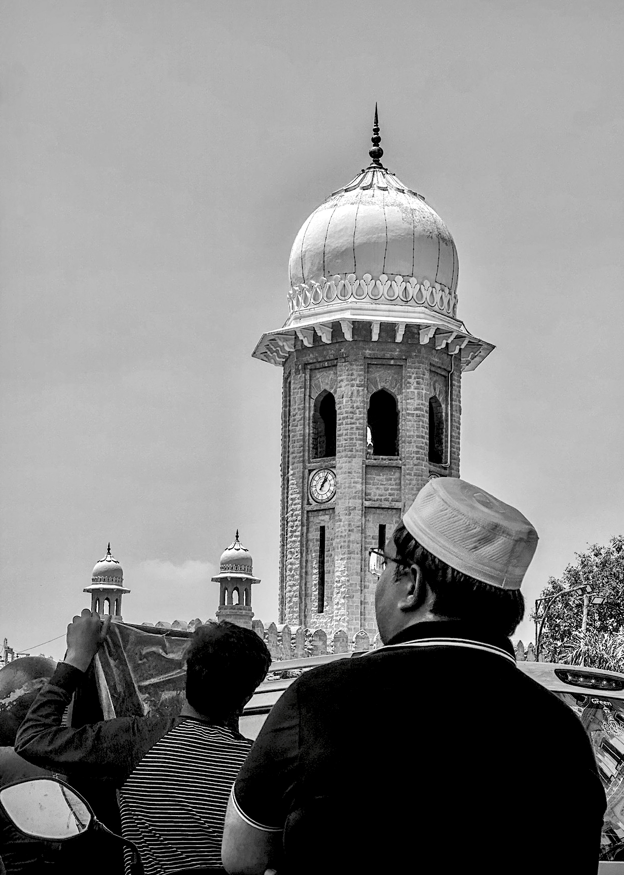 Two people viewing tall minaret with clock tower from below - human scale architectural photography